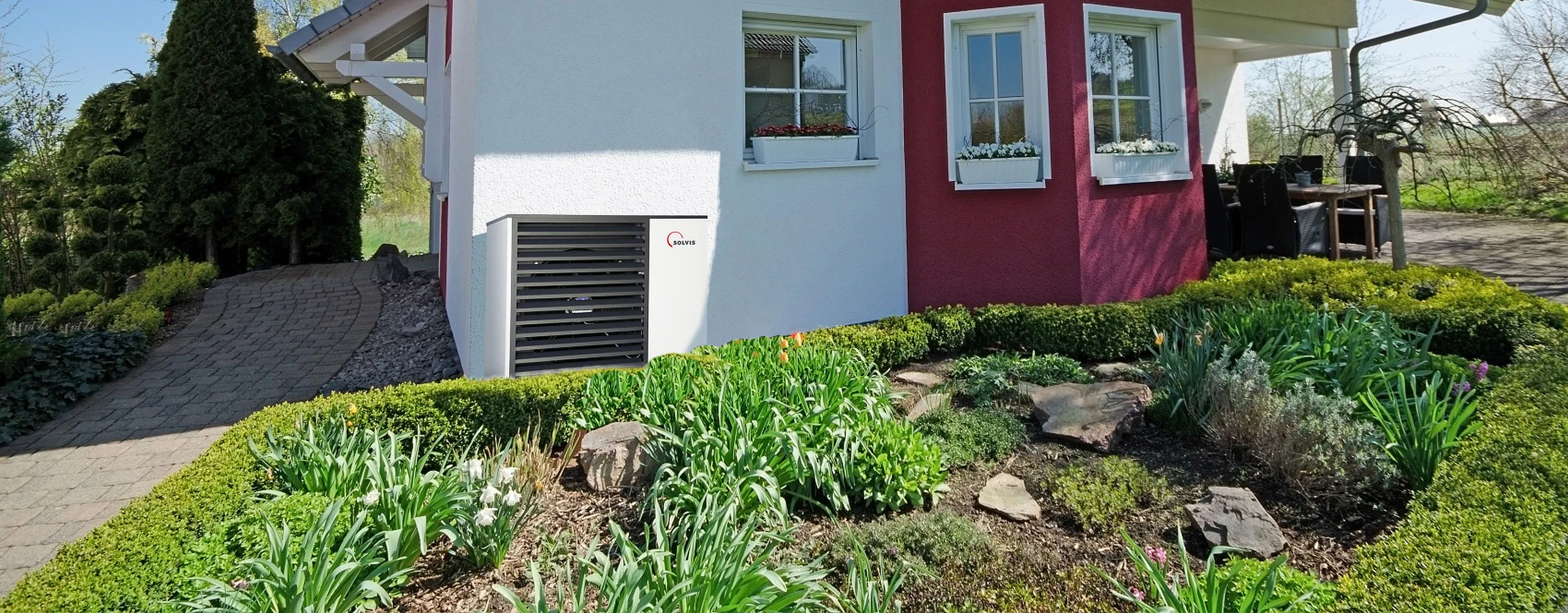 Wärmepumpe SolvisMia vor kleinen Einfamilienhaus mit Garten.