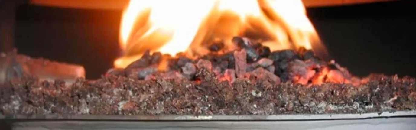 Nahaufnahme von glühender Kohle in einem Ofen, über der eine Flamme lodert.