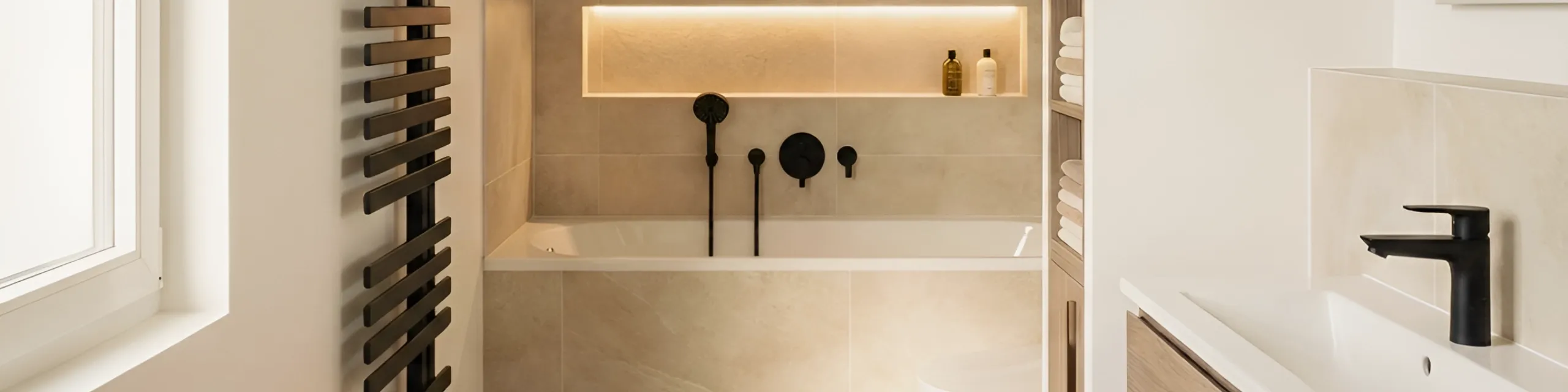 Zeitloses Badezimmerdesign mit heller Fliesenoptik, schwarzer Waschtischarmatur und stilvoller Beleuchtung über der Badewanne.