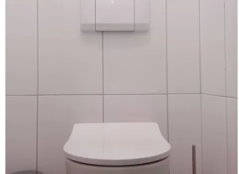 Weiße Toilette im weißgefliesten Bad.