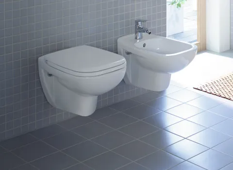 Helles Badezimmer mit einem wandhängenden WC und einem stilvollen weißen Bidet, beide an einer gefliesten Wand befestigt.