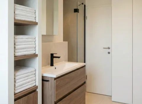 Waschplatz mit Unterschrank in Holzoptik, schwarzem Wasserhahn und integrierten Handtuchregalen aus Holz.