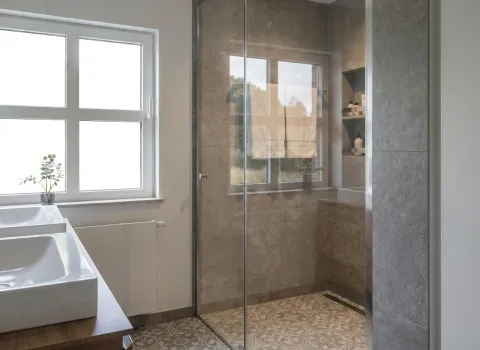 Tageslichtbad mit großem Fenster, begehbarer Dusche und integrierten Wandnischen für Duschutensilien.