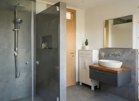 Badezimmer mit begehbarer Dusche, Aufsatzwaschbecken auf Holzplatte und minimalistischer Einrichtung.