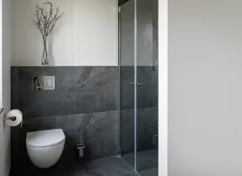 Kompaktes Badezimmer mit wandhängendem WC, bodengleicher Dusche und grauen Natursteinfliesen.