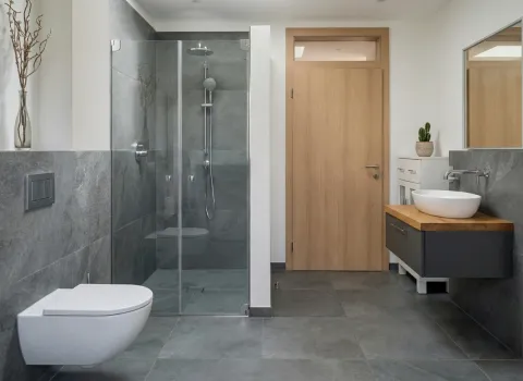 Badezimmer mit grauen Feinsteinzeugfliesen, begehbarer Dusche, Holzdetails und minimalistischer Einrichtung.