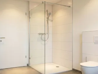 Dusche mit Glaswand, weißen Fliesen und Vorwandarmatur.