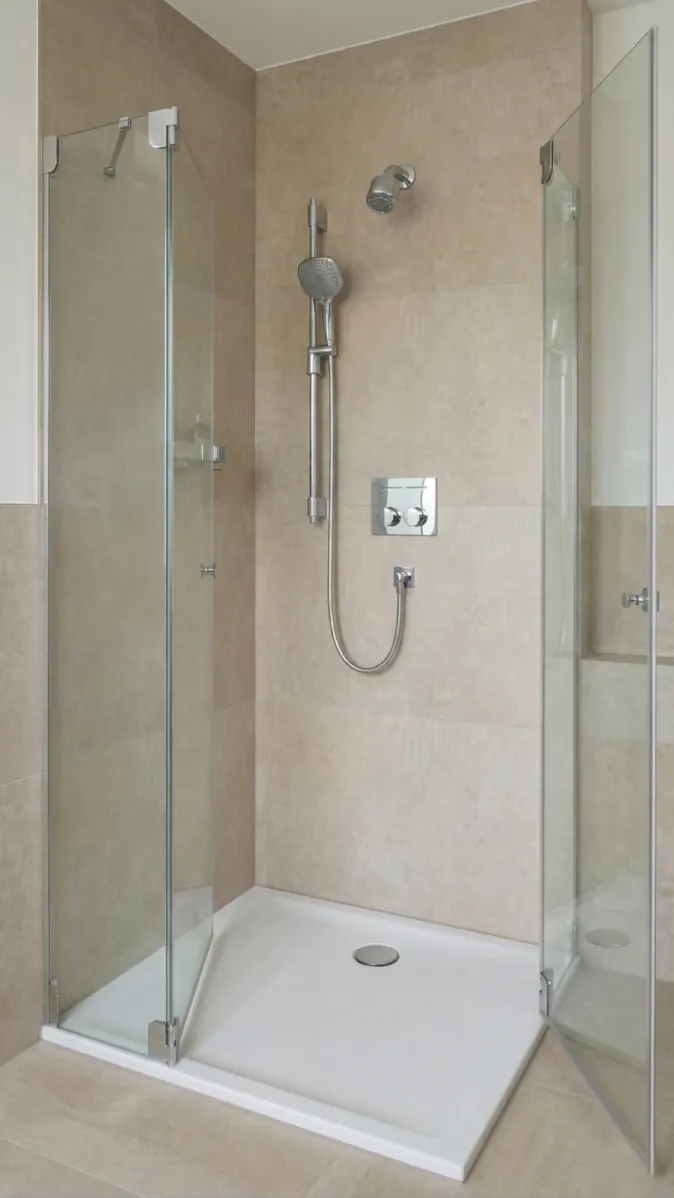 Minimalistische Duschkabine mit Doppeldusche und rahmenlosen Glastüren auf weißer Duschwanne.