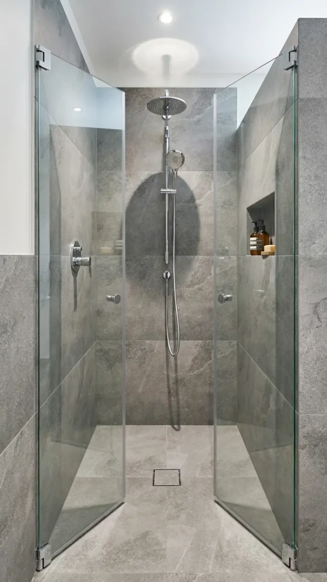 Begehbare Dusche mit Regendusche, grauen Fliesen und Nische für Pflegeprodukte.