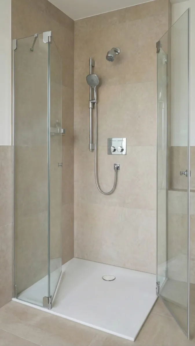 Minimalistische Duschkabine mit Doppeldusche und rahmenlosen Glastüren auf weißer Duschwanne.