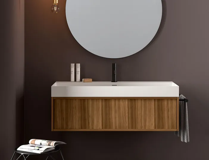 Elegantes Badmöbel von Stocco mit Holzunterschrank, rundem Spiegel, schwarzer Armatur und dunkler Wandfarbe im modernen Stil.
